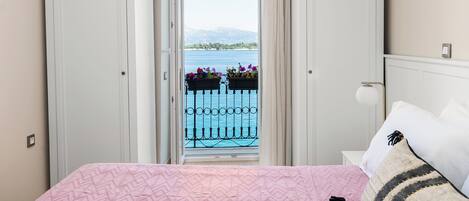 A bedroom with a bed, a nightstand, and a window with a view of a balcony and water.