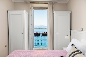 Una camera da letto con un letto, un comodino e una finestra vista balcone e mare.