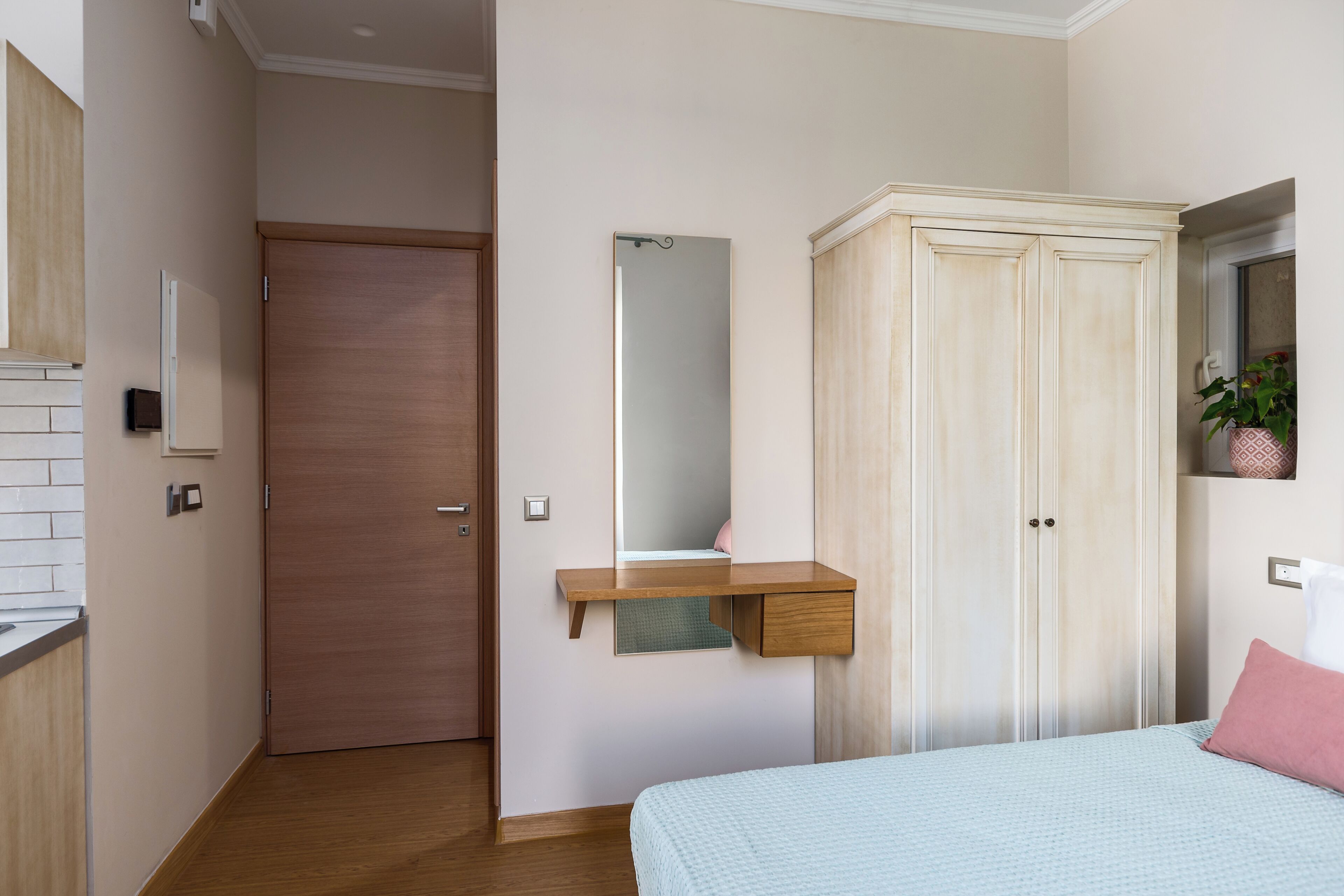 Ein Schlafzimmer mit einem Bett, einem Kleiderschrank, einem Spiegel und einem kleinen Schreibtisch mit Ablagefläche.