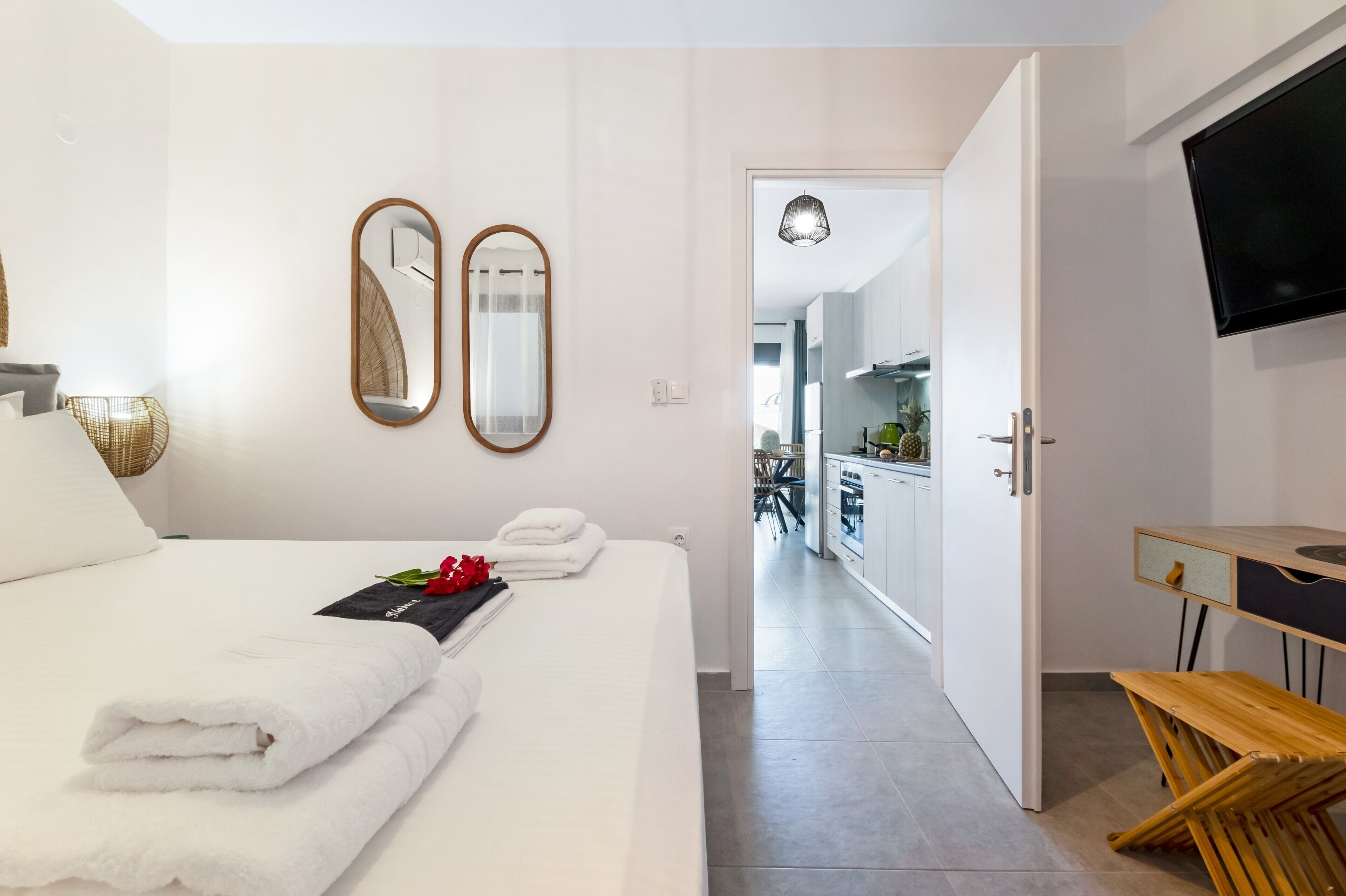 Een hotelkamer met een bed, twee spiegels, een televisie, een houten bureau en uitzicht op de keuken.