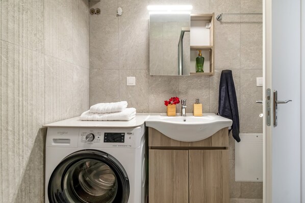 A modern bathroom with a washing machine, sink, mirror, and wooden cabinets.