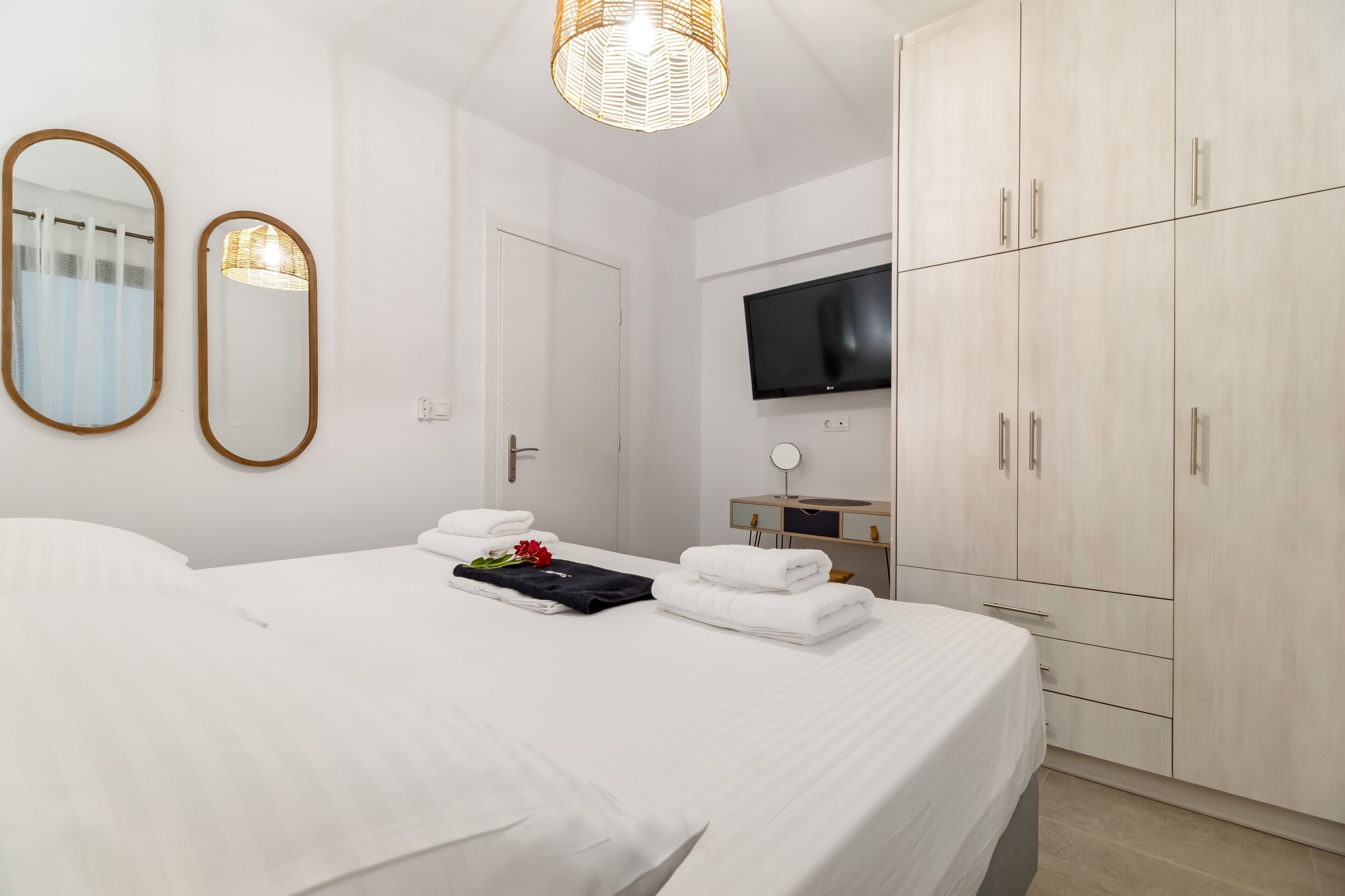 A hotel room with a bed, two mirrors, a television, and a wardrobe.