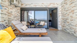 A modern lounge area with a sofa, chairs, and a table, a large sliding glass door, and a stone-textured wall. - Studio Apartment 'Oceanida Terpsis Lyxury Suite' with Sea View, Wi-Fi and Air Conditioning (Lefkada)