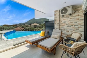 A rooftop terrace with a swimming pool, lounge chairs, and a view of the surrounding landscape.