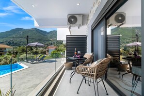 A balcony with a pool, wicker chairs, a table with a bottle, and a view of mountains.