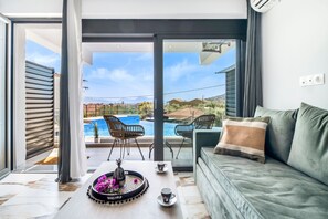 En moderne stue med sofa, sofabord med bakke og blomster, samt udsigt til en swimmingpool og bjerge.