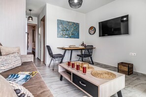 A modern living room with a sofa, a coffee table, a dining area with chairs, a TV mounted on the wall, and a painting.