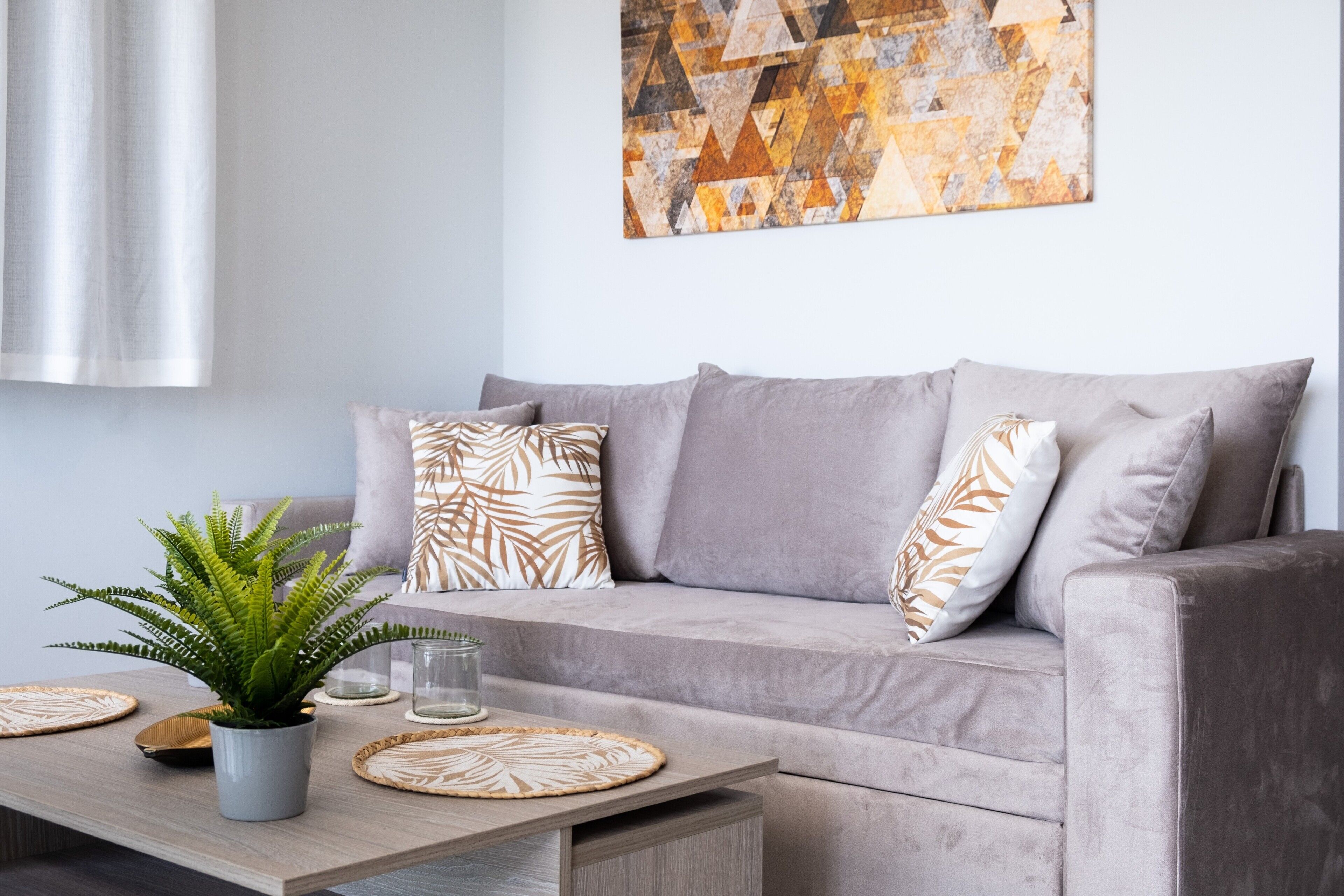 Un soggiorno moderno con un divano grigio, cuscini decorati, una pianta in vaso e un quadro astratto al muro.