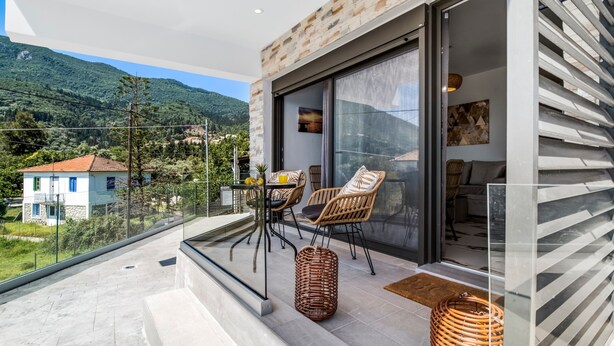 A balcony with wicker furniture, a glass door leading to a room, and a view of a mountain. - Studio Apartment 'Oceanida Thalia Lyxury Suite' with Sea View, Wi-Fi and Air Conditioning (Lefkada)