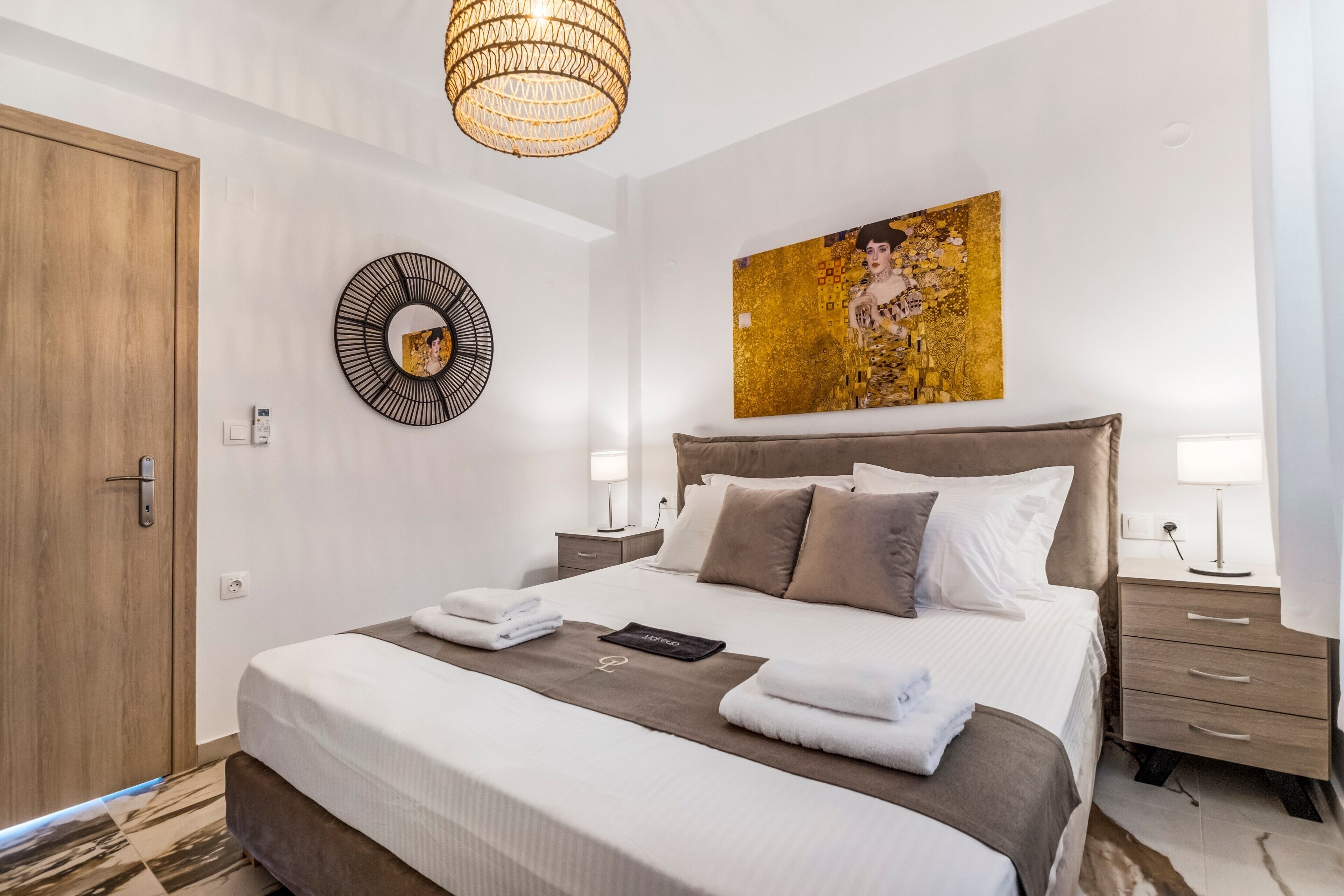 Ein Hotelzimmer mit einem großen Bett, einer Holztür, einem runden Spiegel, einem Gemälde und einem Nachttisch mit einer Lampe.