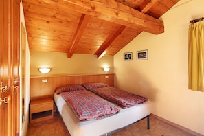 A bedroom with a wooden ceiling, two bedside lamps, a bed with plaid bedding, and a yellow curtain.