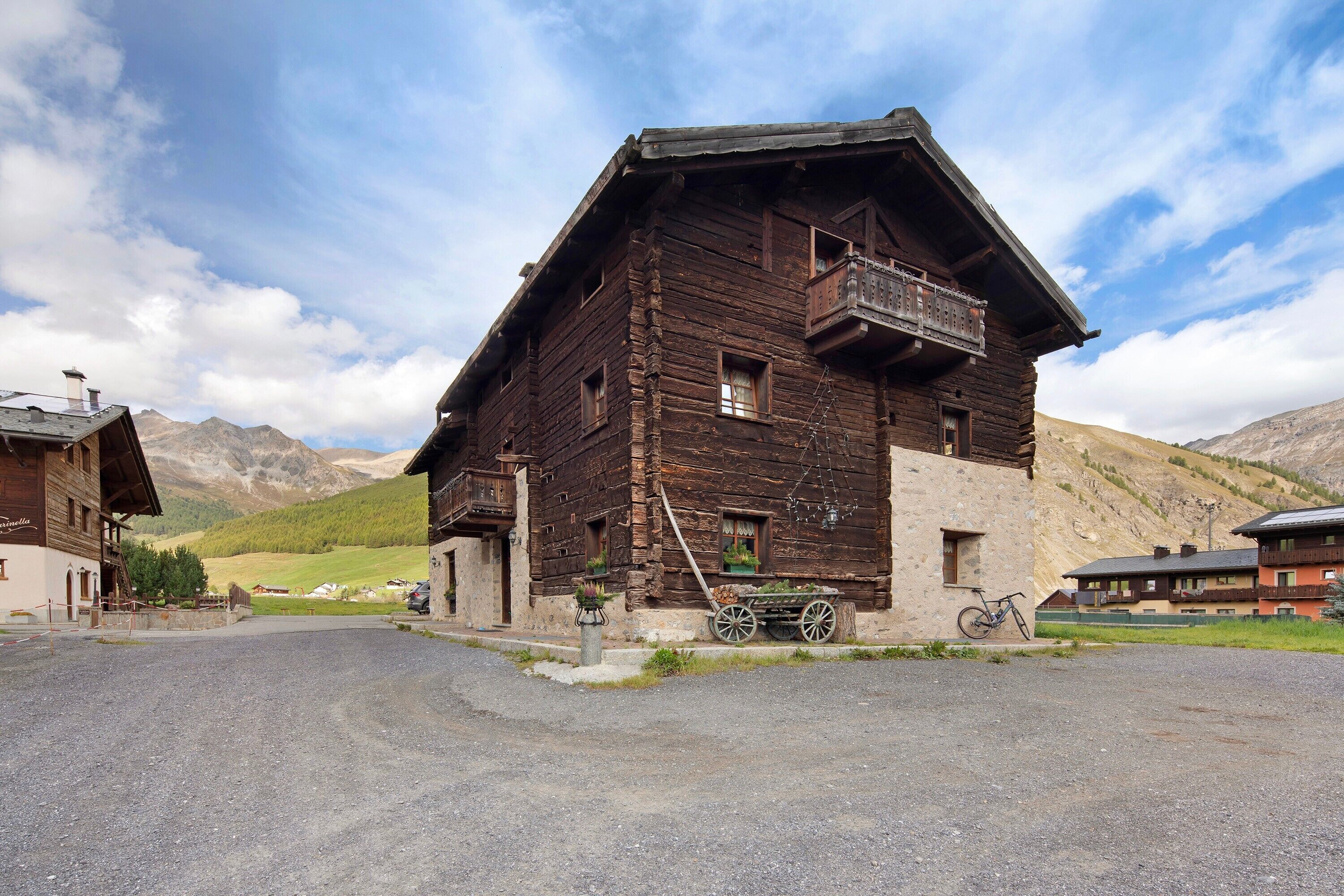 A rustic wooden building with a balcony, a bicycle, and a cart in front.