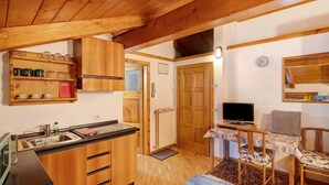 A compact kitchen with wooden cabinets, a sink, and a small dining area with a table and chairs. - Studio 'Campacc Lia' with Mountain View, Shared Garden and Wi-Fi (Livigno)