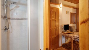 A bathroom with a shower, a wooden door, a bed with a TV, and a clock on the wall. - Studio 'Campacc Lia' with Mountain View, Shared Garden and Wi-Fi (Livigno)