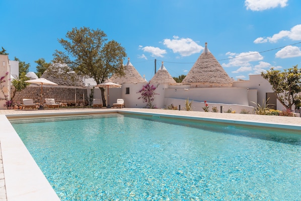 Una piscina con lettini e ombrelloni, circondata da edifici bianchi con tetti a cono.