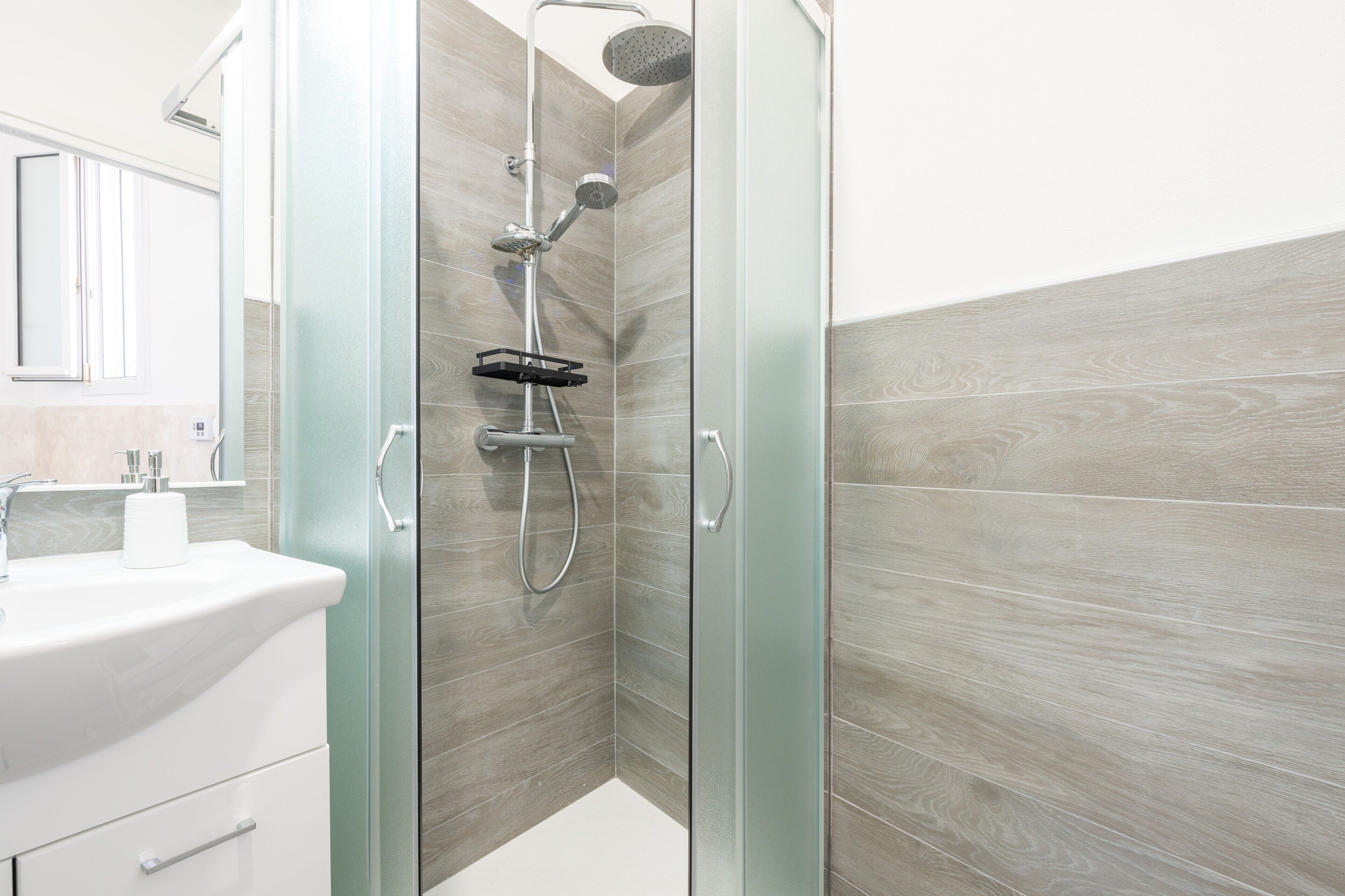 Un baño moderno con cabina de ducha de vidrio, un lavabo blanco y un espejo.