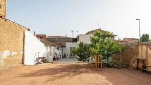 A courtyard with a dirt ground, a brick wall, a white building, and a tree. - Holiday Home 'Casa Manu' with Private Terrace, Wi-Fi and Air Conditioning (Assemini)