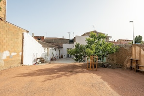 A courtyard with a dirt ground, a brick wall, a white building, and a tree. - Holiday Home 'Casa Manu' with Private Terrace, Wi-Fi and Air Conditioning (Assemini)
