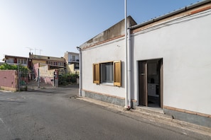 A building with a white exterior, a wooden door, and a window with wooden shutters. - Holiday Home 'Casa Manu' with Private Terrace, Wi-Fi and Air Conditioning (Assemini)