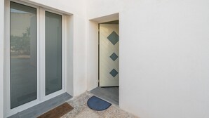 A narrow hallway with a door leading to a room, a window with a view of the outside, and a mat at the entrance. - Holiday Home 'Casa Manu' with Private Terrace, Wi-Fi and Air Conditioning (Assemini)