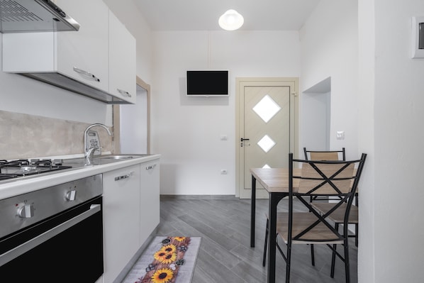A modern kitchen with a stove, sink, and a flat-screen TV mounted on the wall.