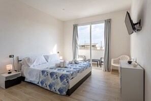 A bedroom with a bed, bedside table, lamp, and a view of the outside.