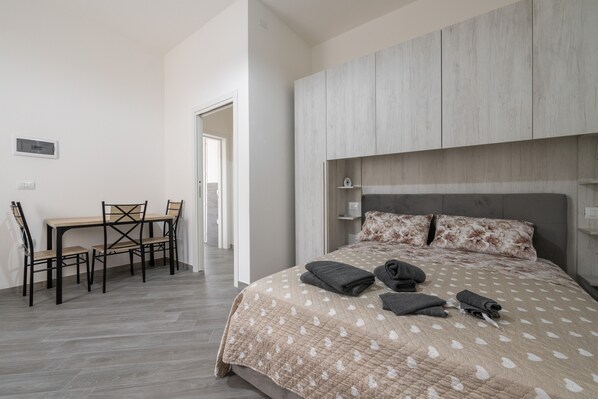 A bedroom with a bed, a bedside table, a chair, and a desk.
