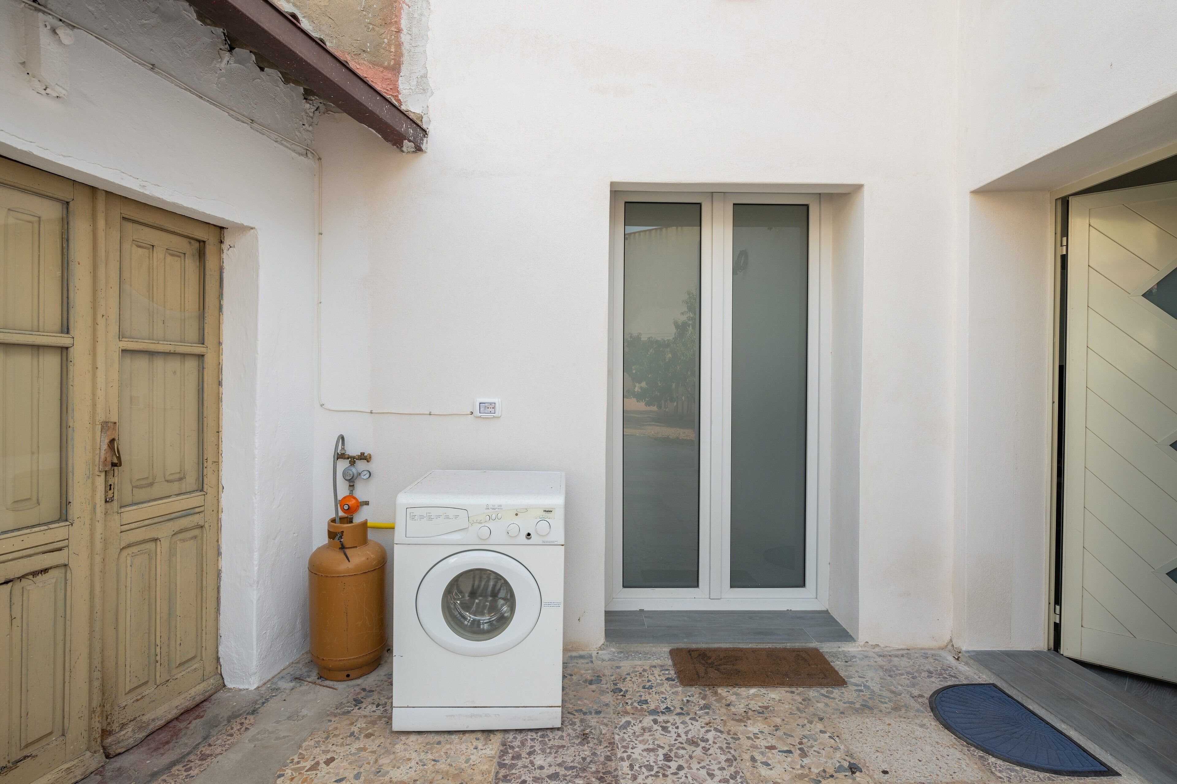 A laundry area with a washing machine, a gas cylinder, and a door leading to a covered entrance.