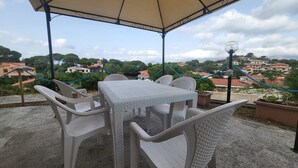 An outdoor patio with a table and chairs, a blue rope barrier, and a view of a residential area with houses and trees. - Apartment 'Spiagge Bianche' with Sea View, Balcony and Air Conditioning (Portoferraio)