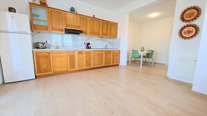 A kitchen with wooden cabinets, a white refrigerator, and a dining area with a table and chairs. - Apartment 'Spiagge Bianche' with Sea View, Balcony and Air Conditioning (Portoferraio)