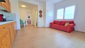 A spacious living area with a red sofa, wooden cabinets, and a kitchen area with a red appliance. - Apartment 'Spiagge Bianche' with Sea View, Balcony and Air Conditioning (Portoferraio)