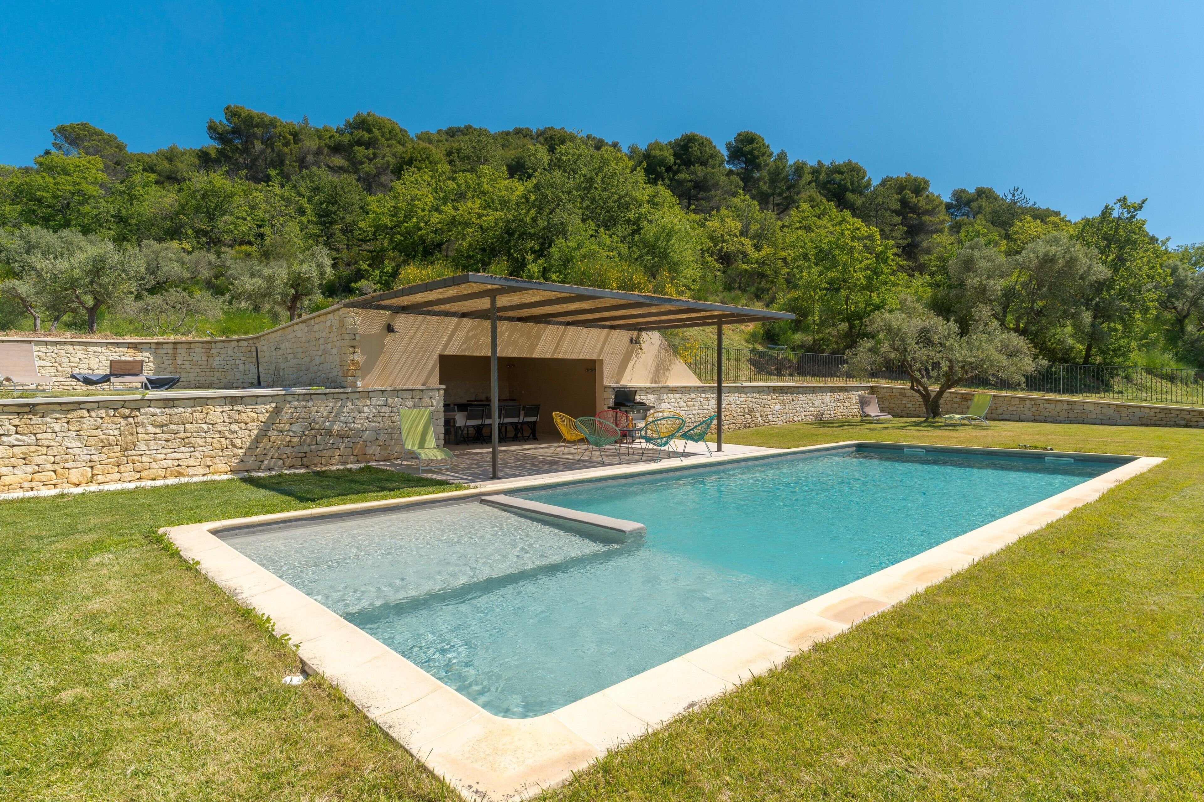 Una piscina rettangolare con una parete in pietra e un'area patio coperta.