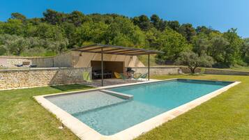 Una piscina rettangolare con una parete in pietra e un'area patio coperta.