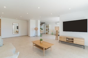 A spacious living area with a wooden coffee table, a flat-screen TV, and a staircase leading to another level.