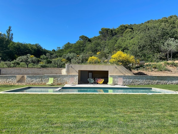 A swimming pool with a stone wall and a small building with an open door.
