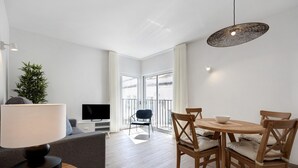 A modern living room with a sofa, a dining table with chairs, a TV, and a large window.