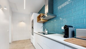 A modern kitchen with white cabinets, a blue backsplash, a built-in oven, and a coffee machine.