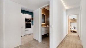 A modern kitchen with built-in appliances, a wooden accent wall, and a narrow hallway leading to a bedroom with a bunk bed.