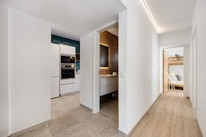 Eine moderne Küche mit integrierten Geräten, einer Wand in Holzoptik und einem schmalen Flur, der zum Schlafzimmer mit Etagenbett führt.