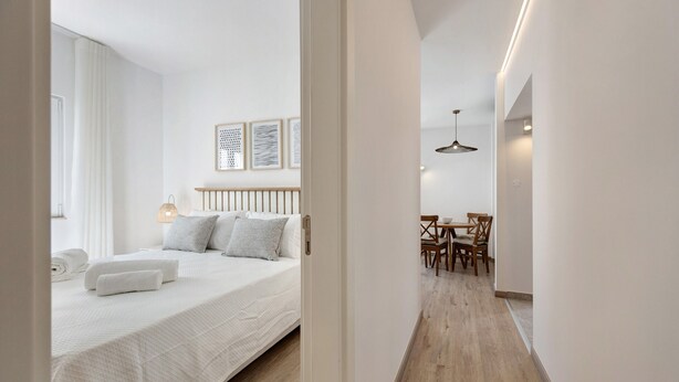 A hotel room with a bed, a bedside table, a lamp, a chair, and a dining table with chairs.