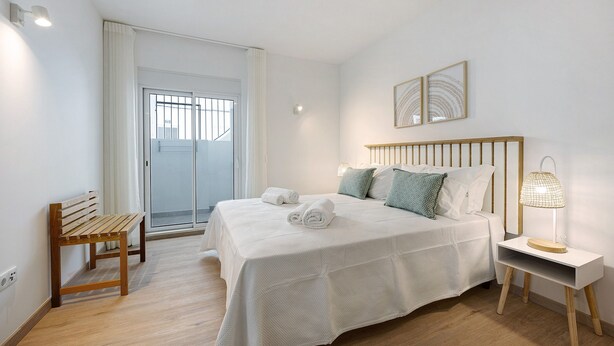 Een slaapkamer met een bed, een bankje, een nachtkastje met een lamp en een deur die leidt naar een balkon.