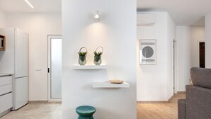 Een moderne keuken met witte kasten, een blauwgroene stoel en een wandplank met decoratieve objecten.