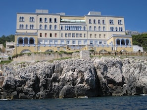 A large building with multiple balconies and arched windows, situated on a rocky coastline.
