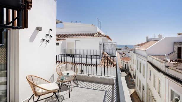 Un balcon avec des fauteuils en osier, une petite table et une vue sur le paysage urbain.