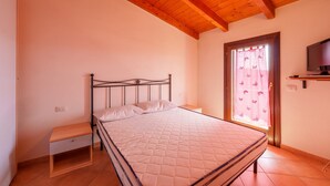 Een slaapkamer met een bed, nachtkastje, televisie en een raam met gordijnen.
