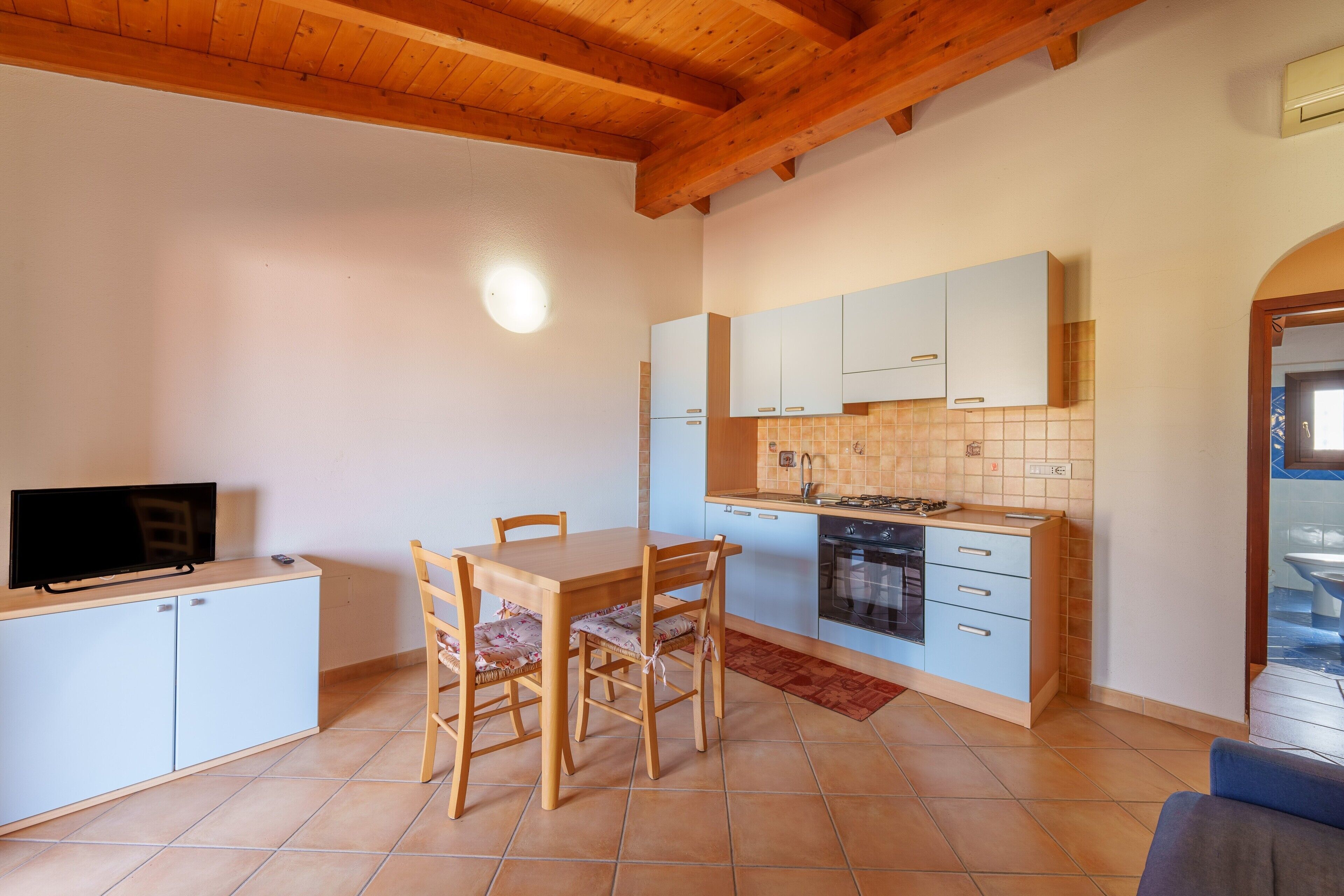 Une cuisine compacte comprenant une table à manger, des chaises, un téléviseur posé sur un meuble et un crédence carrelée.