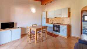 Een compacte keuken met een eettafel, stoelen, een televisie op een kast en een betegelde achterwand.