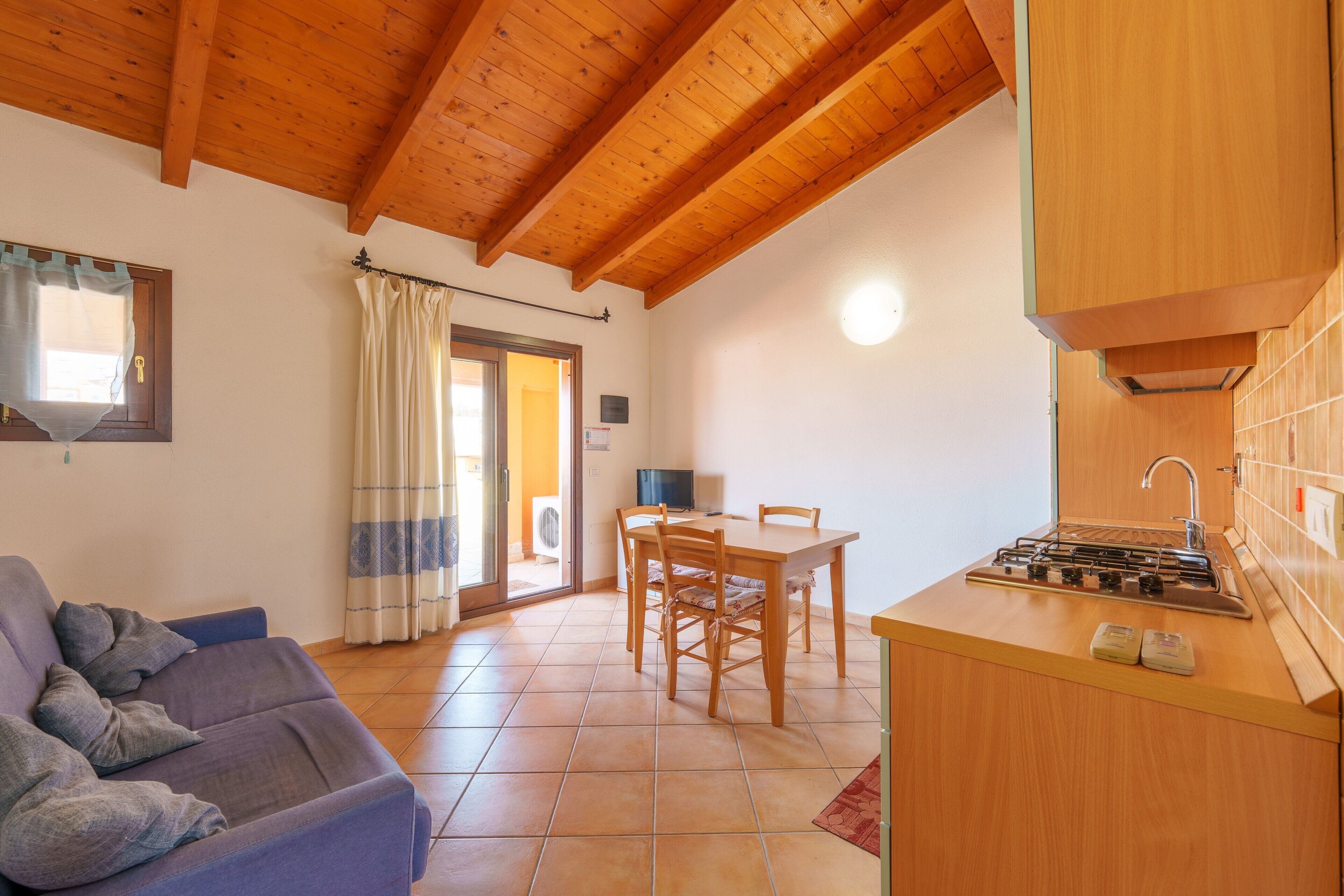 Une pièce chaleureuse avec un plafond en bois, un canapé, une table à manger avec des chaises et un coin cuisine.