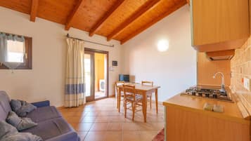 Una habitación acogedora con techo de madera, un sofá, una mesa de comedor con sillas y una zona de kitchenette.