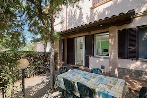 An outdoor patio with a table and chairs, a door, and a window with shutters.